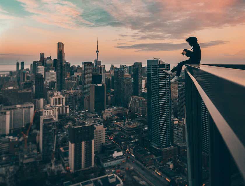 Pessoa sentada no topo de um edifício, observando a paisagem urbana abaixo.