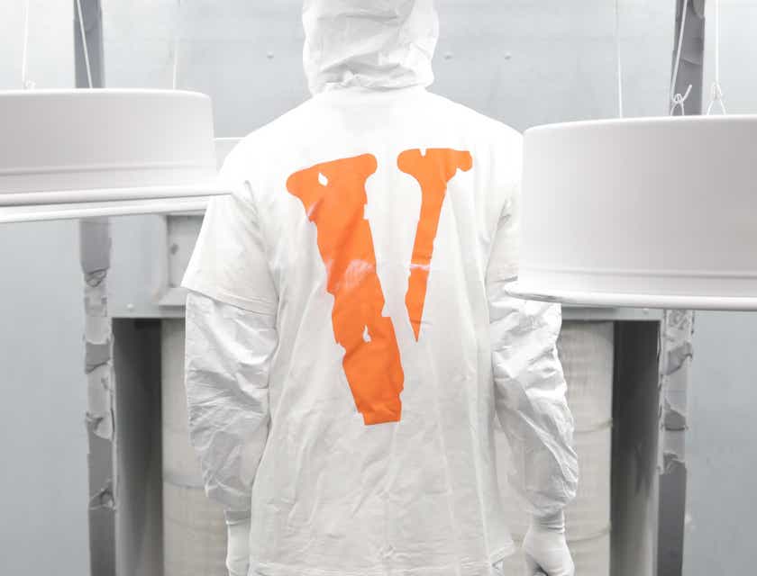 Osoba w białym ubraniu ochronnym z pomarańczową literą „V”.