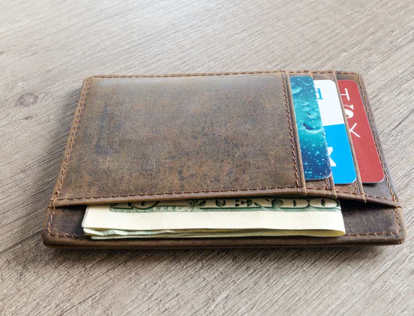 Una cartera marrón que contiene tarjetas de crédito y billetes en dólares estadounidenses en un logo de cartera.