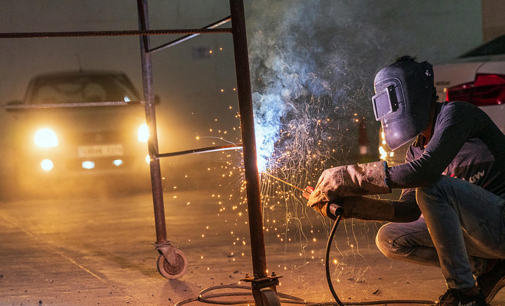 Welder wearing a protective mask and working on a steel ladder in a garage.
